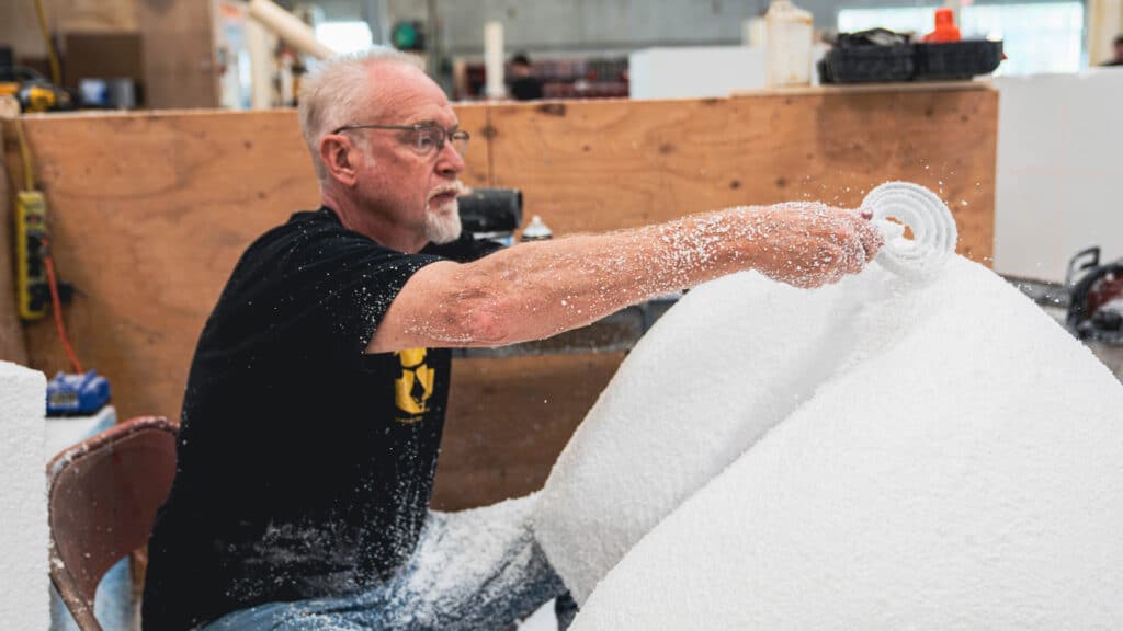Skilled fabricator at Steadfast Displays carving a large foam structure by hand for a custom trade show installation inside a workshop environment.