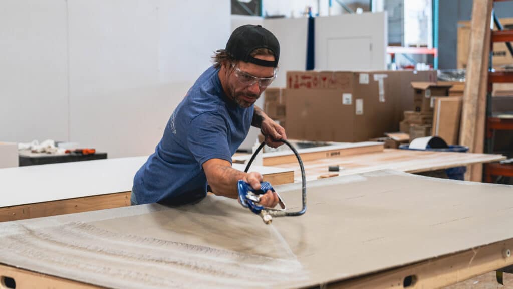 Worker applying spray finish to trade show booth panel inside fabrication facility.